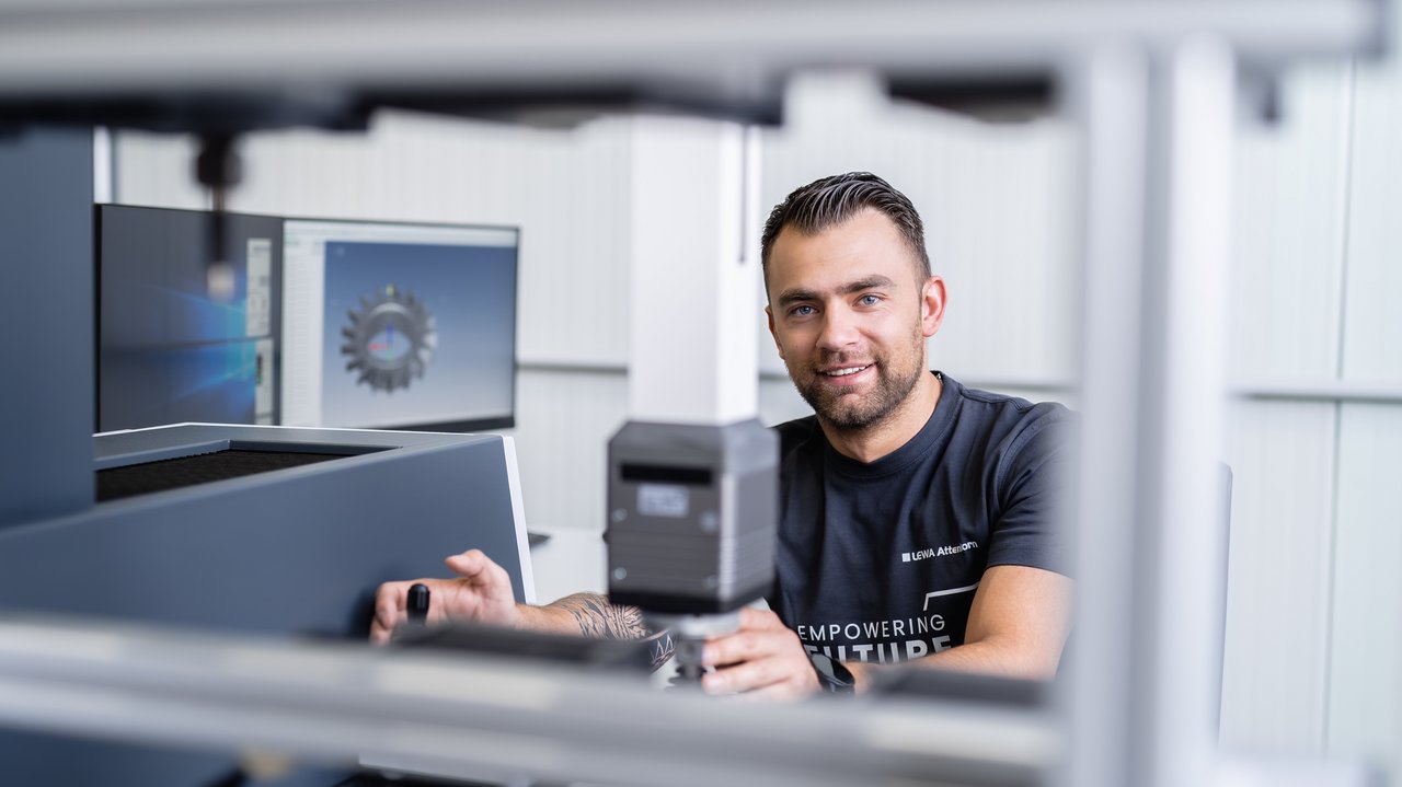 Capacitar a las personas Selbstbewusster junger Mann an Messmaschine, Ausbildung in der Qualitätssicherung bei LEWA Attendorn
